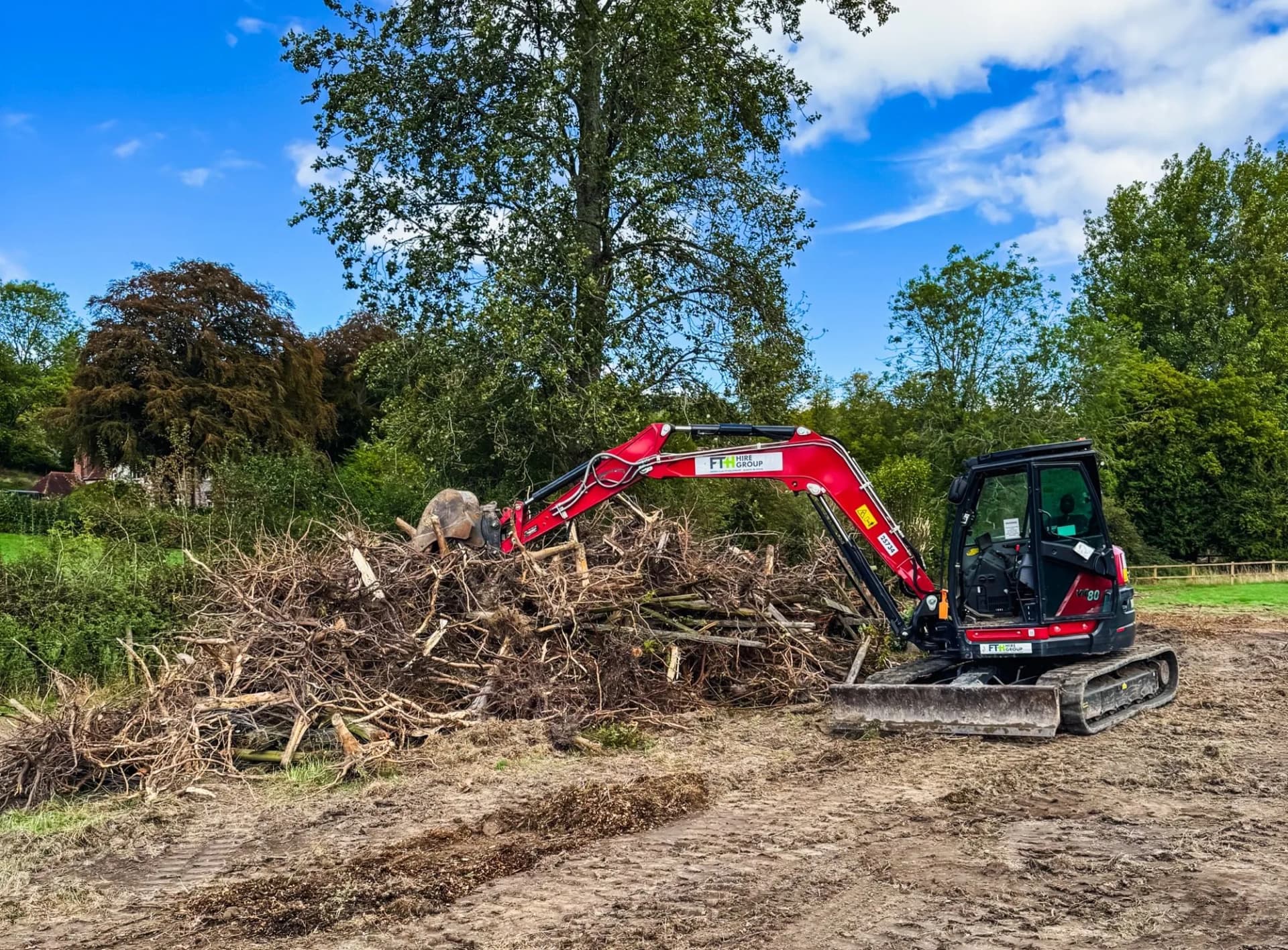 An 8-tonne excavator stacking uprooted tree stumps and root systems into a pile on a cleared East Meon paddock