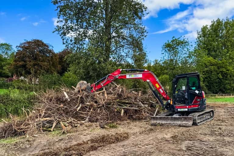 An 8-tonne excavator stacking uprooted tree stumps and root systems into a pile on a cleared East Meon paddock
