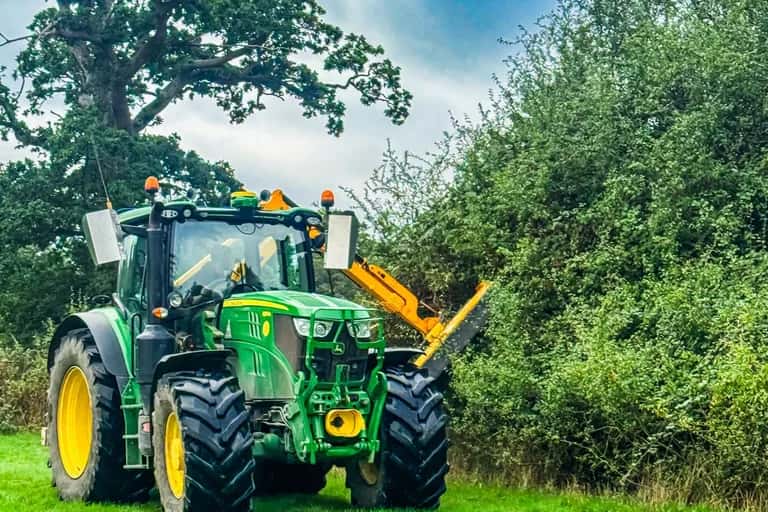 John Deere 6155R tractor fitted with a tractor-mounted hedge cutter beside an overgrown hedge in East Meon